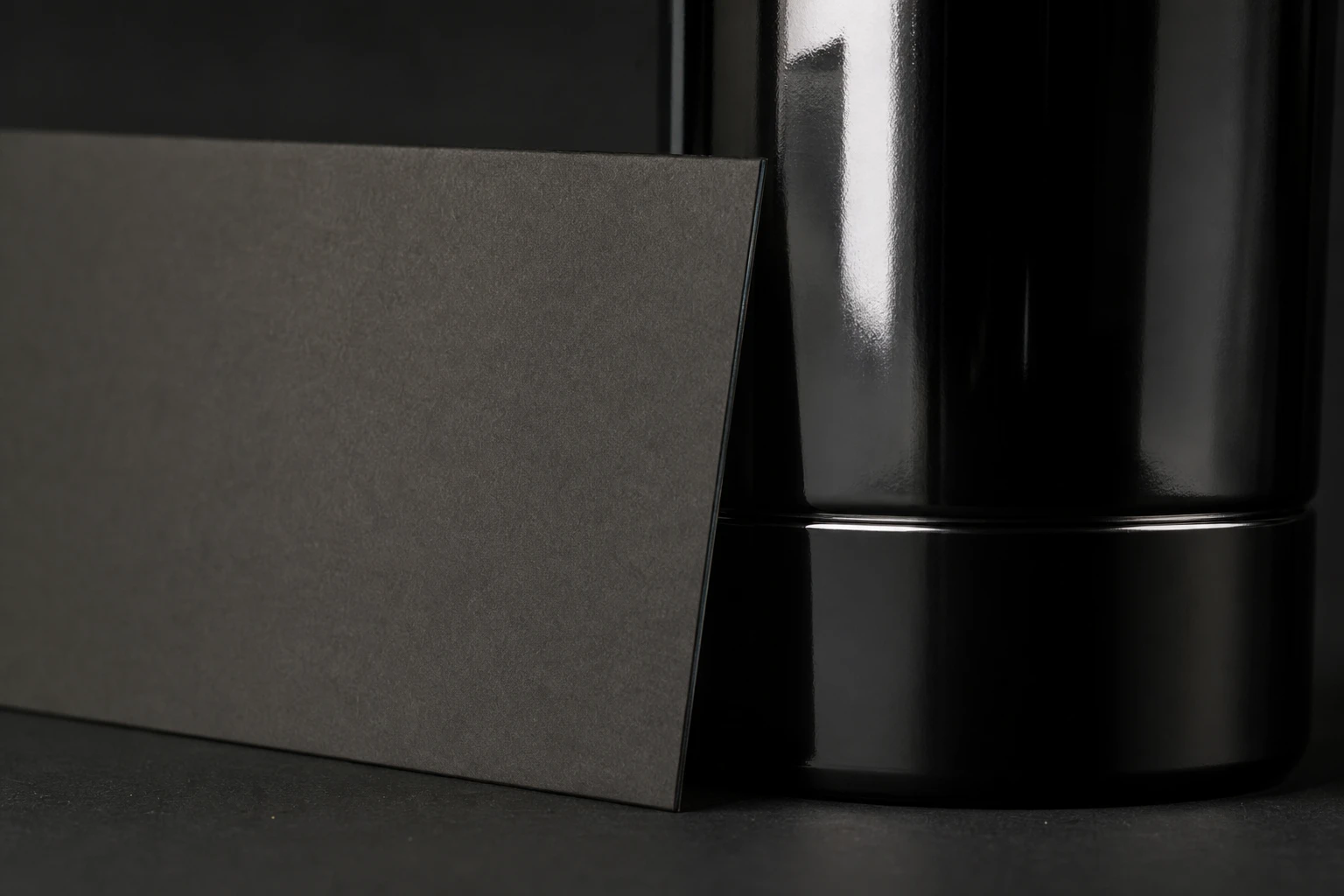 Black card (product), rigged as it is used — Black cards beside glossy packaging carve dark reflection bands — shape without changing lights