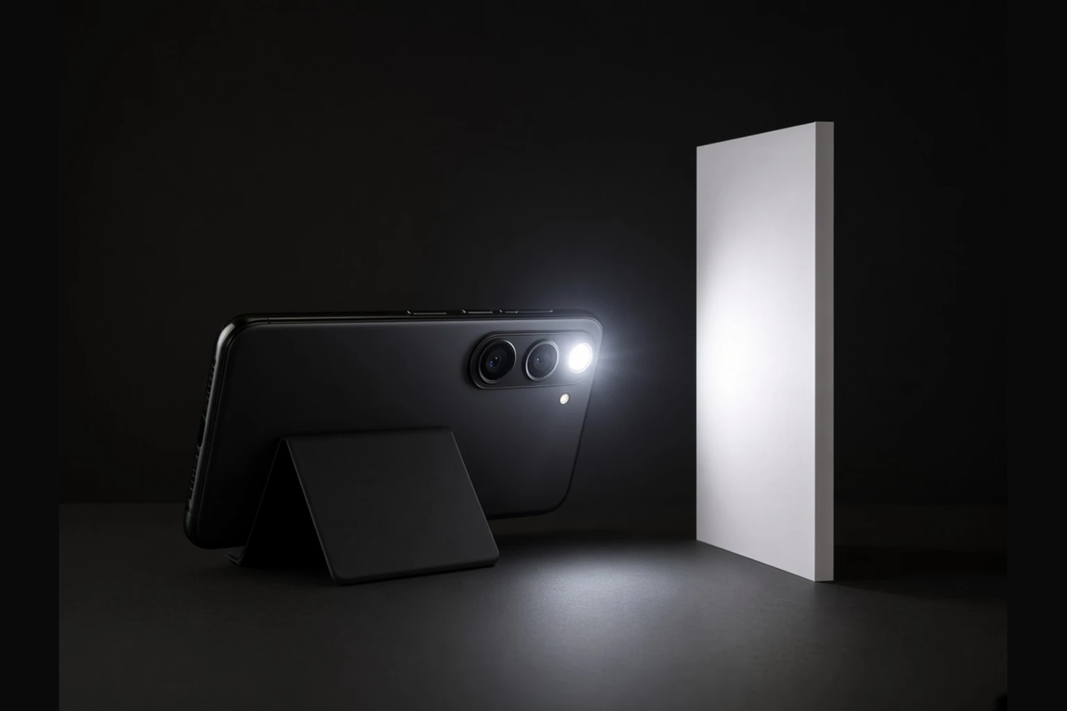 Black smartphone on a kickstand with the rear LED flashlight on, casting a cool hotspot onto a white board